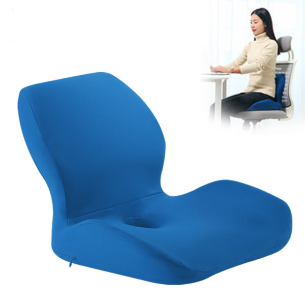 Coussin en forme de L bleu vu de profil. Derrière se trouve une femme brune habillée en blanc qui travaille à un bureau. Elle est assise sur une chaise de bureau avec un coussin bleu derrière elle.