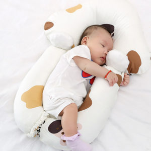 Matelas ergonomique pour caler bébé lors de ses nuits. Bébé dedans sur le côté avec body blanc et chaussettes rose. Motif tâches marrons et jaunes sur les rebords rembourrés du matelas.