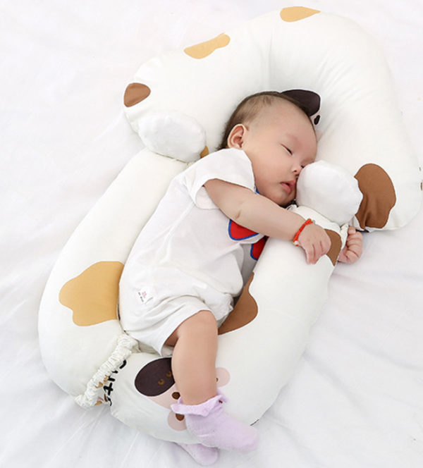 Matelas ergonomique pour caler bébé lors de ses nuits. Bébé dedans sur le côté avec body blanc et chaussettes rose. Motif tâches marrons et jaunes sur les rebords rembourrés du matelas.