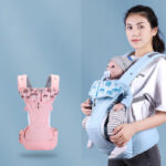 Porte bébé rose à gauche et bleu à droite avec bébé qui porte une tétine dedans. La maman sourit.