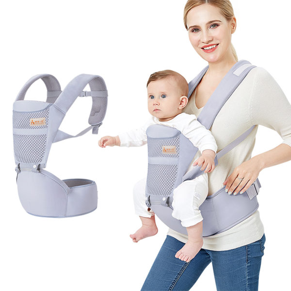 Bébé en combinaison blanche dans son porte bébé gris clair porté par sa maman qui sourit.