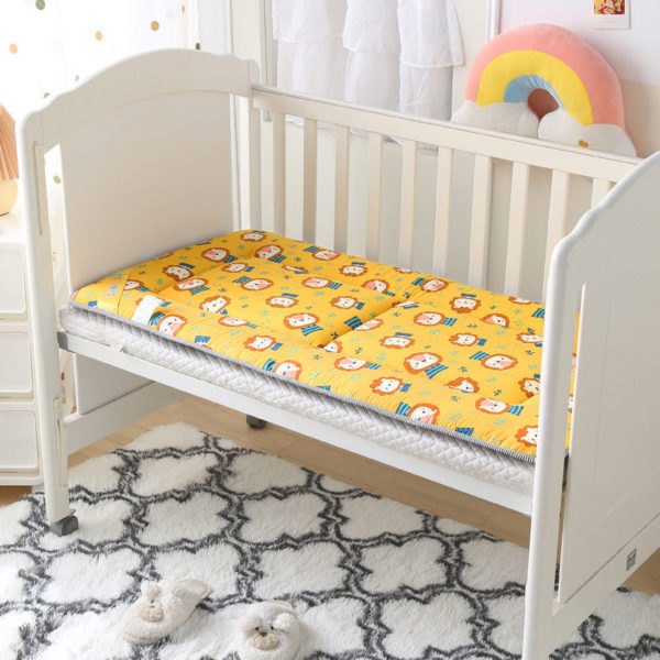 Matelas ergonomique jaune à tête de lion pour lit de bébé. Installé dans un lit blanc à barreaux. Arc en ciel en peluche au dessus et tapis à motif blanc et noir en dessous