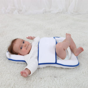 Matelas ergonomique anti-renversement à scratch blanc aux coutures bleues marines. Bébé avec bras en l'air et pied sur genou de l'autre jambe.