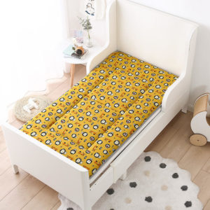 Matelas ergonomique jaune aux motifs d'inspiration savane. Dans lit blanc, tapis rond au sol sur parquet.
