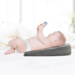 Oreiller ergonomique dodo pour bébé en mousse gris. Bébé allongé en couche avec bras levés jambes croisées.