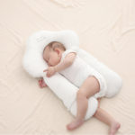 Oreiller ergonomique dodo pour bébé blanc en forme de nuage. Avec bébé qui dort sur le côté en body blanc.