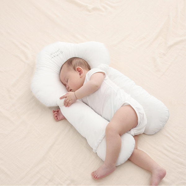 Oreiller ergonomique dodo pour bébé blanc en forme de nuage. Avec bébé qui dort sur le côté en body blanc.