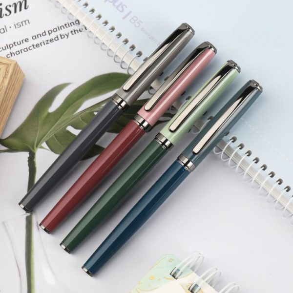 quatre stylos sont posés sur des cahiers blanc et bleu. Les stylos sont rose, vert, bleu, gris.