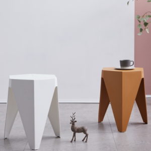 2 tabourets contemporains posés dans une pièce. Une tasse est posée sur le tabouret orange. Une figurine cerf est posée sur le sol gris. Mur blanc en fond.