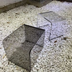 2 tabourets transparents sur un sol de galets blancs.