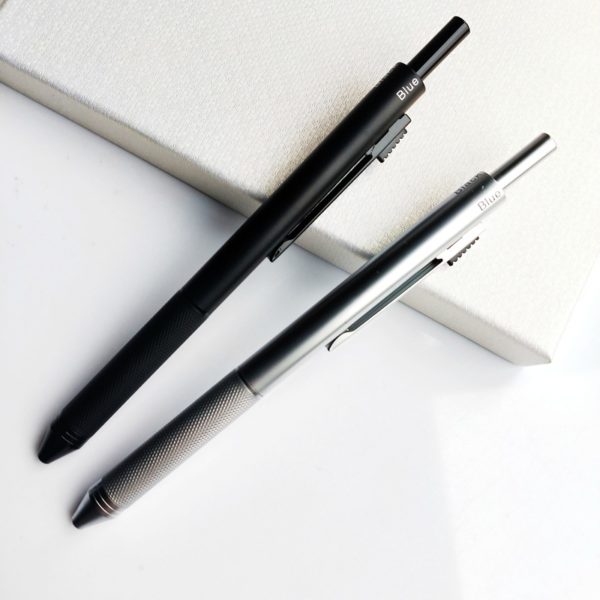 un stylo noir et un stylo gris sont posés sur un objet blanc le tout sur une table blanche