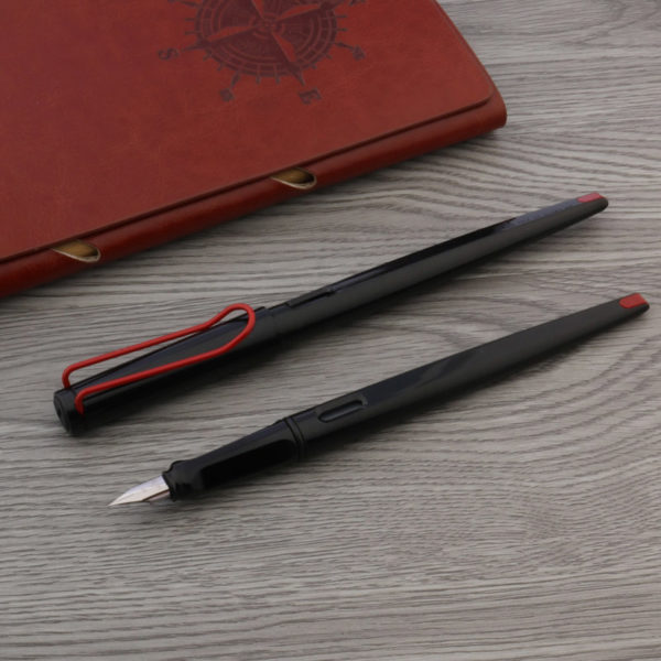 Deux stylos noir et rouge sont posés sur une table en bois. Un des stylos a un bouchon l'autre non. Un classeur en cuir marron se trouve à côté.