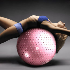 Femme allongée sur un ballon rose au revêtement dentelé, sur fond gris.