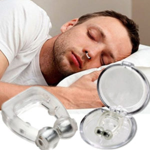 Homme qui dort sur un oreiller blanc avec au premier plan une boite en plastique avec un pince nez en silicone et des aimants