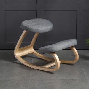 Chaise grise ergonomique avec assise à genoux et cadrant en bois. Il est placé sur un fond gris.