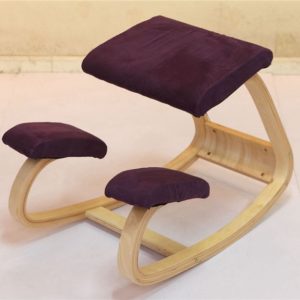 Ce siège ergonomique assis à genoux est violet et en bois. Il est placé sur un sol gris et dans le fond se trouve un mur beige
