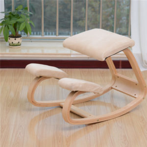 Un siège ergonomique beige assis à genoux est placé au milieu d'une pièce. Le sol de la pièce est en bois. Il y a une fenêtre au fond avec une plante verte.