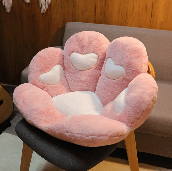 Sur une chaise en bois avec un revêtement gris, on voit un coussin d'assise rose et blanc en forme de patte de chat.