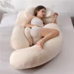 Une femme allongée sur un gros coussin de grossesse beige sur un lit gris.