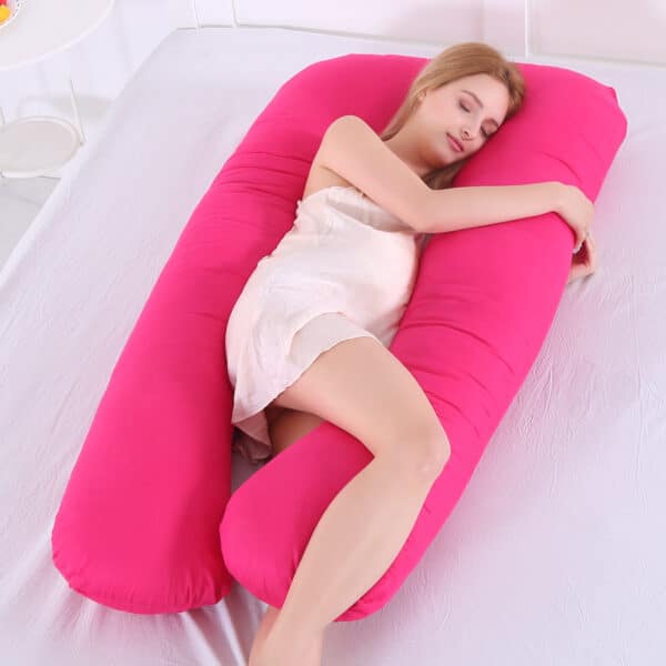 Une femme allongée sur une grand coussin rose sur une surface grise.