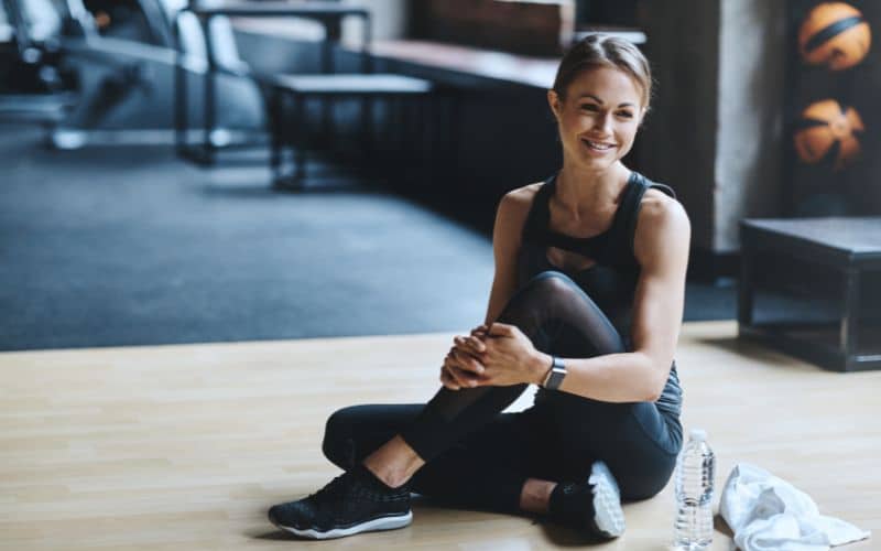 Femme assise au sol en tenue de sport, souriante.