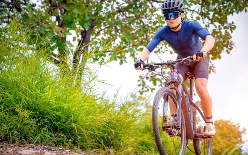 Pourquoi Choisir des Poignées de VTT Ergonomiques : Avantages pour les Cyclistes Homme sur un VTT dans la nature portant un casque et des lunettes de soleil.