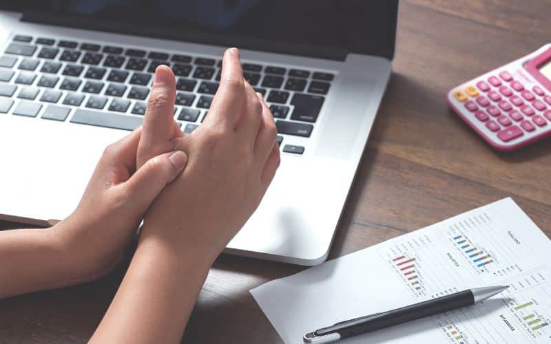 Personne devant son ordinateur portable, se tenant la main droite à un point qui semble douloureux.