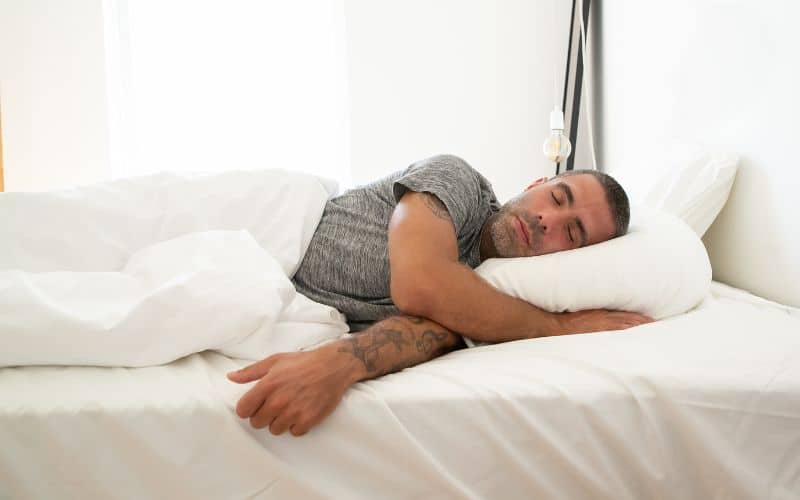 Homme allongé dans son lit, la tête sur un coussin chauffant.