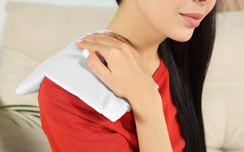 Femme, avec un coussin chauffant sur l'épaule pour soulager sa douleur.