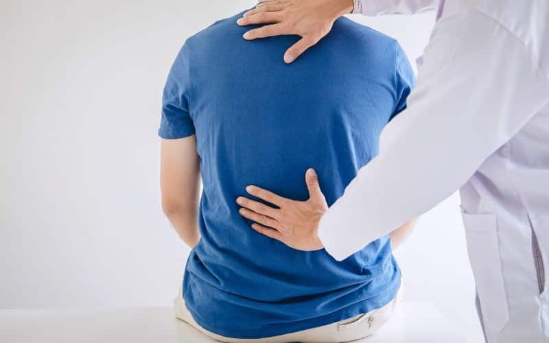 Homme de dos assis, avec les mains d'un médecin posées sur le dos.