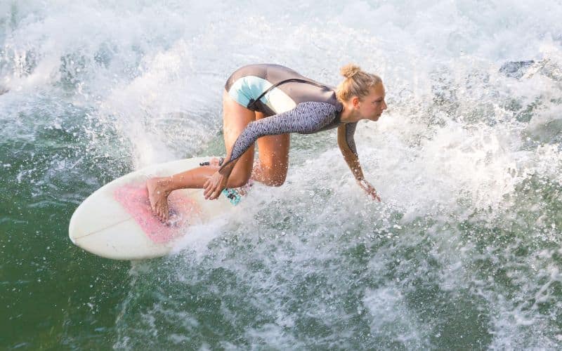 Surfeuse sur une vague, avec planche de surf ergonomique et tenue de surf ergonomique.