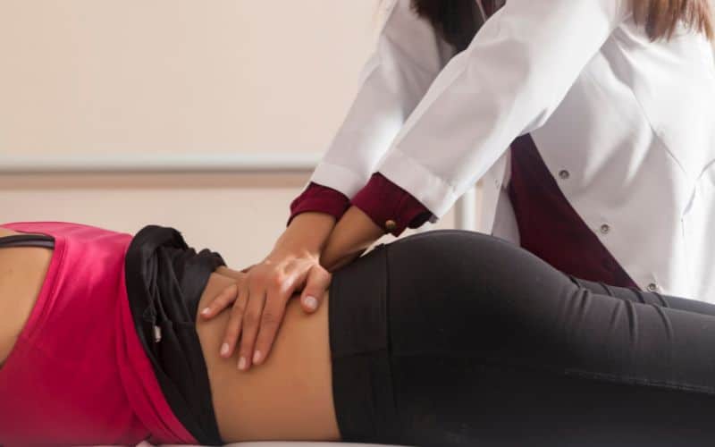 Femme thérapeute qui masse le dos d'une personne allongée sur le ventre.