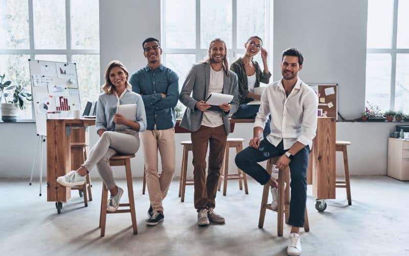 Que dit la loi sur l'ergonomie au travail ? Groupe de personne qui travaillentensembles,à côté d'une table et de tabourets hauts.
