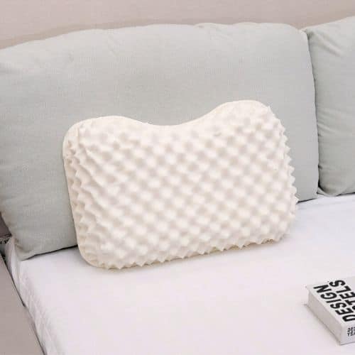 Oreiller latex naturel : guide pour choisir le meilleur latex Oreiller latex végétal à texture en nid d’abeille, blanc, posé sur canapé beige, livre adjacent. Oreiller latex naturel déployant son confort ergonomique.